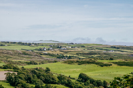 Scenic view of green rolling hills and scattered rural houses in the picturesque countryside under a bright cloudy sky