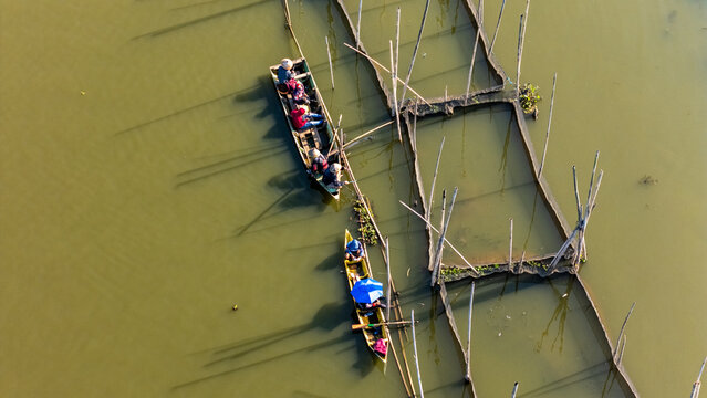 Aerial view of fishermen in wooden boats navigating through fish farming cages on a lake in Salatiga, Central Java, Indonesia.