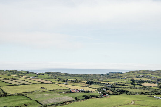 Scenic aerial view of green patchwork fields and rolling hills in the rural countryside with the ocean on the distant horizon under a bright sky