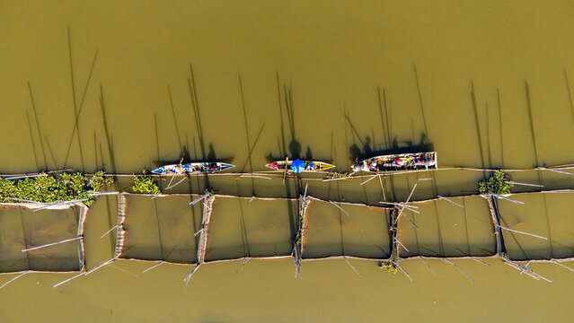 Aerial view of fishermen in small wooden boats navigating between traditional fish farming nets in the calm water of Salatiga, Central Java, Indonesia.