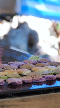 Vertical video. Street food vendor pouring raw batter onto a hot flat griddle surface to prepare traditional Thai coconut pancakes Khanom Babin