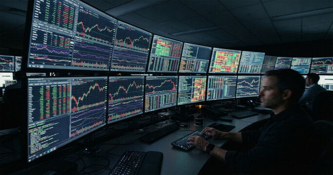 Stock trader working in dark control room analyzing financial charts on multiple monitors