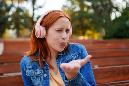 Redhead woman having fun outdoors, expressing playfulness and listening to music with wireless headphones