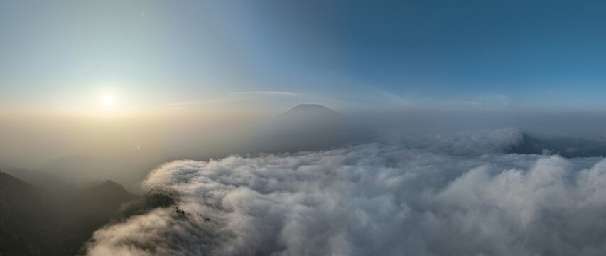 Aerial view of Triangle Sky Telomoyo at sunrise with a sea of clouds surrounding the mountain peak in Kecamatan Ngablak, Jawa Tengah, Indonesia.