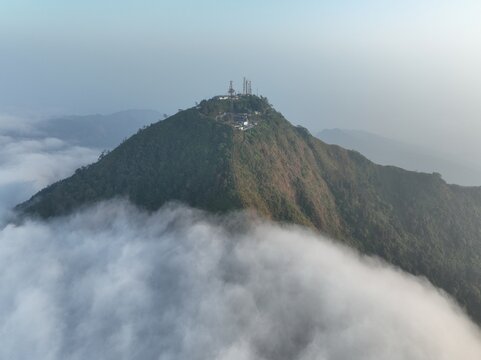 Aerial view of Triangle Sky Telomoyo peak rising above a sea of clouds with communication towers and lush green slopes in Kecamatan Ngablak, Jawa Tengah, Indonesia.