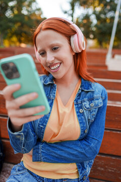 Young woman connecting with smartphone, listening to music with wireless headphones and smiling outdoors