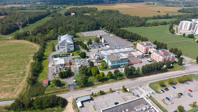 Aerial view of the STMicroelectronics semiconductor manufacturing facility surrounded by green fields and trees in Cornaredo, Lombardy, Italy.