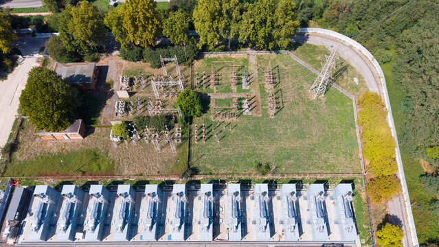Aerial view of a data center with a row of diesel generators and an adjacent electrical substation surrounded by trees in Milan, Lombardy, Italy.