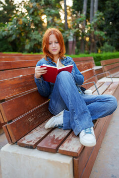 Young woman enjoying a book outdoors, relaxing on a park bench and focusing on her reading