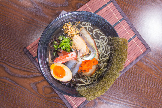 Delicious bowl of ramen with seafood, egg, and toppings served on a wooden table