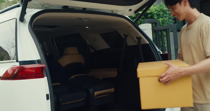 Young Asian couple carries cardboard boxes to load car trunk while moving out. Family relocation home mortgage loan, Real estate moving transport vehicle, New house package delivery pack concept.
