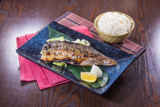 Grilled fish served with rice and lemon on a black plate in a restaurant
