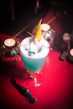 Colorful drink served in a glass on a red table near candles in a dim bar setting