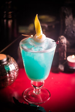 Colorful drink in a glass with ice and a twist of lemon served in a bar during the evening