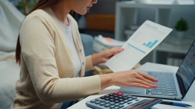 Close up young Asian woman calculates expenses and checks bills with laptop in living room at home. Personal finance budget planning, Tax return invoice paperwork, Household banking savings analysis.