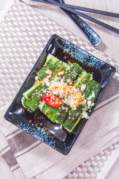 Plate with sliced zucchini and toppings served in a black dish with chopsticks on a woven placemat