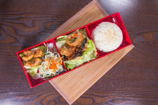 Lunchtime meal served in a red bento box with various dishes on a wooden table