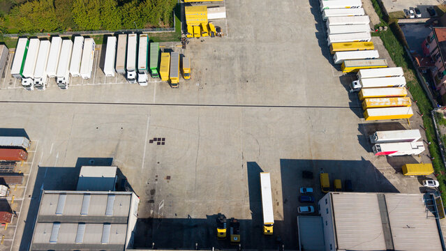 Aerial view of a logistics facility with rows of parked semi-trucks and trailers in a paved yard in Milan, Lombardy, Italy.