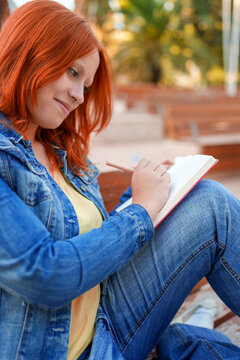 Young woman writing in a notebook with a pencil, focusing on creativity and expressing ideas outdoors