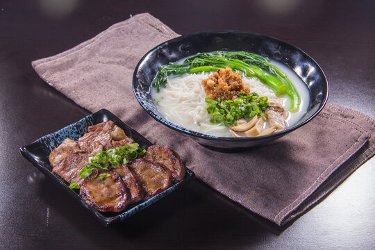 Noodle soup and sliced meat on a dark table with a cloth