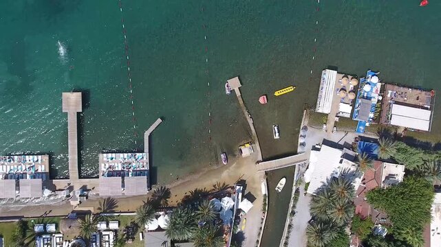 Aerial view moving from a coastal holiday resort with a swimming pool out over the clear blue sea