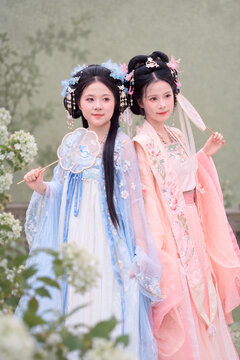 Young women wearing traditional hanfu clothing with fans in garden