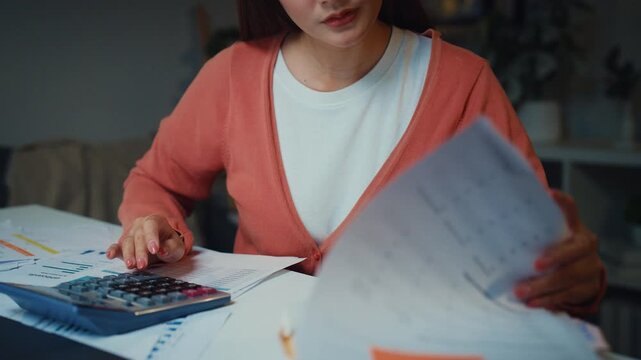 Close up young Asian woman calculates bills and household expenses with calculator and laptop at home at night. Personal finance budgeting, tax payment plan, debt control, savings mortgage management.