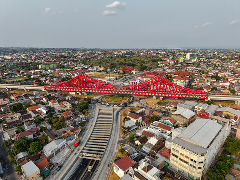 Aerial view of the bright red Jembatan Kereta Api Joglo railway bridge spanning over a busy road intersection and urban landscape in Surakarta, Jawa Tengah, Indonesia.