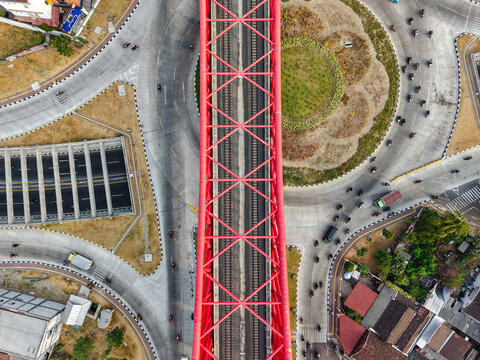 Aerial view of Jembatan Kereta Api Joglo with its distinctive red steel structure spanning over a busy roundabout and railway tracks in the urban landscape Surakarta, Jawa Tengah, Indonesia.