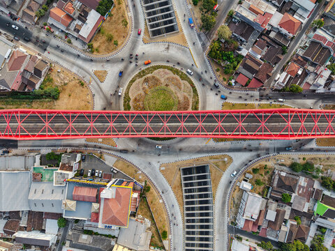 Aerial view of the red Jembatan Kereta Api Joglo railway bridge spanning over a busy roundabout with traffic in Surakarta, Jawa Tengah, Indonesia.