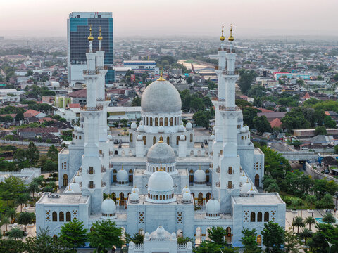 Aerial view of the Sheikh Zayed Grand Mosque with its white marble domes and minarets, surrounded by lush gardens and the urban landscape of Surakarta, Central Java, Indonesia.