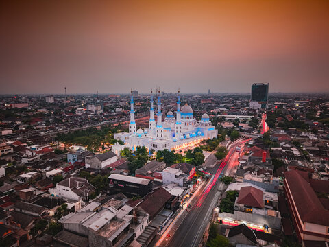 Aerial view of Sheikh Zayed Grand Mosque Solo illuminated at dusk with surrounding city rooftops and light trails on the road in Surakarta, Central Java, Indonesia.