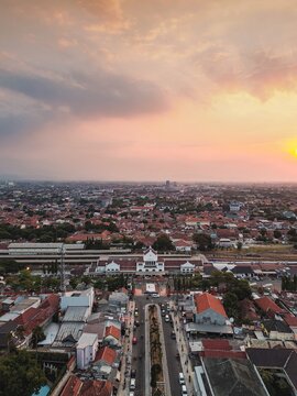 Aerial view of Stasiun Kejaksan surrounded by the dense urban landscape of Cirebon at sunset, featuring terracotta rooftops and railway tracks, Cirebon, West Java, Indonesia.
