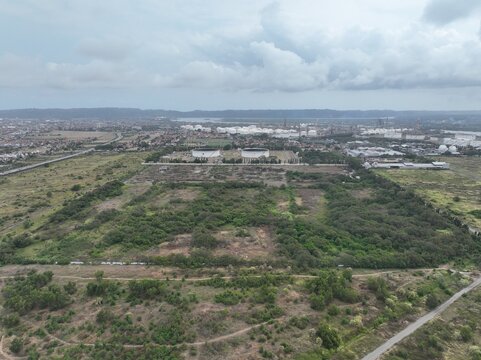 Aerial view of the industrial refinery area with large storage tanks surrounded by green fields and urban landscape in Cilacap, Central Java, Indonesia.