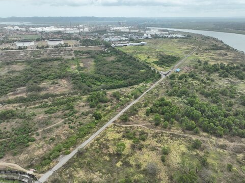 Aerial view of the industrial refinery complex with large oil storage tanks situated near the river, surrounded by lush green vegetation and a dirt road in Cilacap, Central Java, Indonesia.