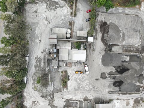Aerial view of an industrial cement plant featuring tall silos, large piles of raw materials, and construction vehicles on the site in Cilacap, Central Java, Indonesia.