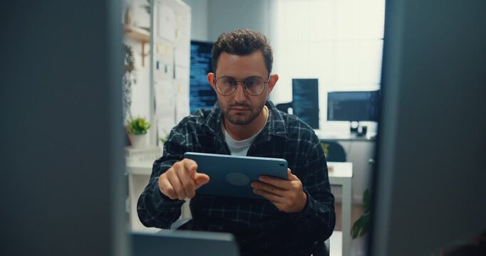 Young Caucasian male developer uses digital tablet to inspect software coding algorithms at office desk. Programming development, Artificial intelligence machine learning, Secure database concept.