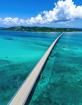A long bridge stretches across clear turquoise waters towards a lush green island under a bright blue sky with fluffy clouds.