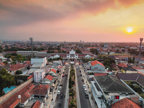 Aerial view of Stasiun Kejaksan featuring historic colonial architecture, urban rooftops, and tree-lined streets during a warm golden hour in Cirebon, West Java, Indonesia.