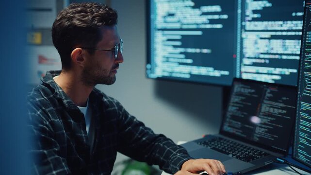 Young Caucasian male programmer write code on computer in home office at late night. AI technology, cybersecurity, software developer, freelance innovation, database system, digital network concept.