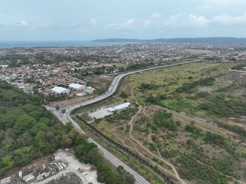 Aerial view of the coastal landscape and highway infrastructure winding through residential areas and green fields in Cilacap Regency, Central Java, Indonesia.