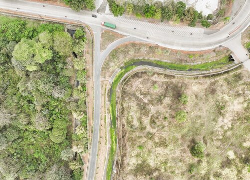 Aerial view of a road junction with a truck, a winding canal, dense forest, and dry vegetation in Cilacap Regency, Central Java, Indonesia.