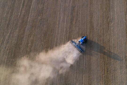 The Blue Agricultural Sprayer Traversing a Vast Field While Emitting Dust Trail