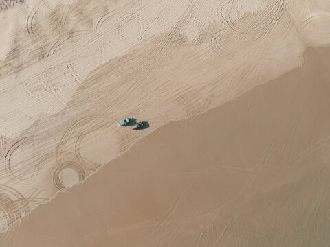 Aerial view of Birubi Point sand dunes featuring intricate tire tracks and two vehicles parked on the vast sandy landscape in Anna Bay, New South Wales, Australia.