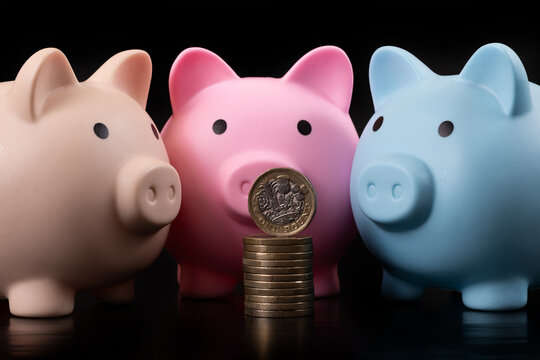 A 1 British pound coin and  colorful piggy banks on a black background.