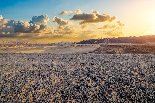 Vast arid desert landscape with rocky ground under golden sunset sky in Dahaidao, Xinjiang, China