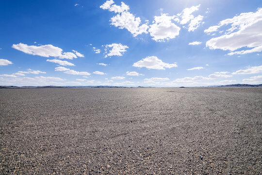 Vast gravel desert plain under a clear blue sky with white clouds in Xinjiang, China