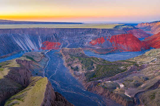 Aerial view of a winding braided river flowing through a deep rocky gorge at sunset in Anjihai Grand Canyon, Xinjiang, China