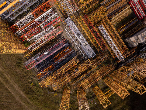 Aerial view of stacked construction crane lattice booms in yellow, red, and white metal arranged in a geometric pattern at an industrial yard in Gdansk, Poland.