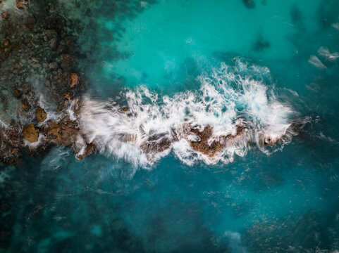 Aerial view of waves crashing against the rocky coastline of Blue Lagoon Nusa Ceningan in Kecamatan Nusa Penida, Bali, Indonesia.